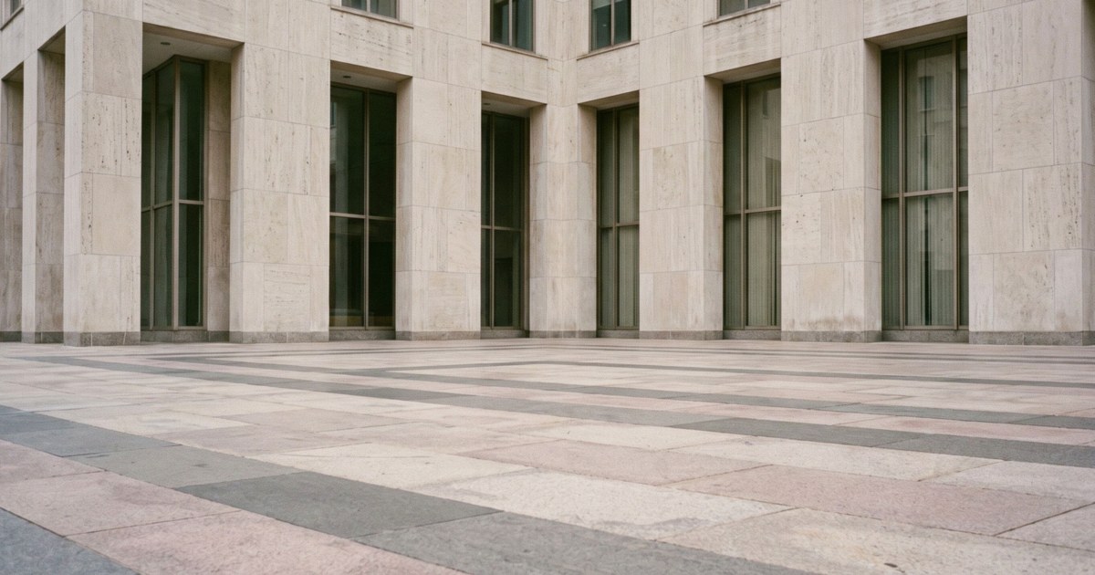 The limestone facade and tall windows of a government office building above an empty stone plaza under soft overcast light.