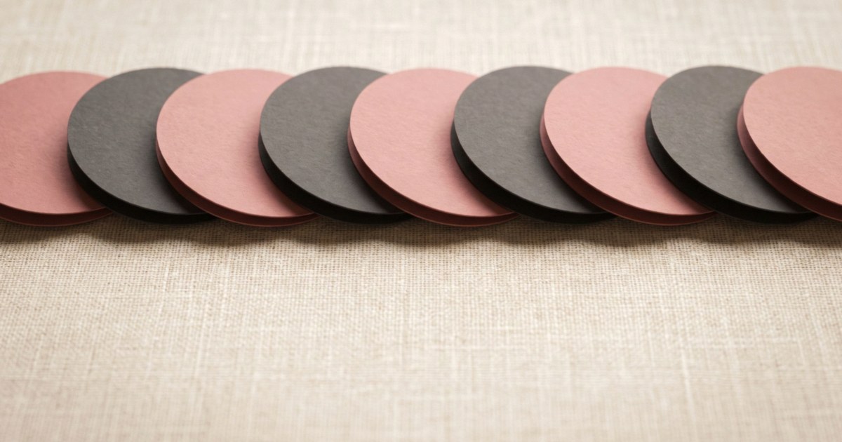 A row of overlapping paper discs alternating dusty rose and charcoal on a linen background.