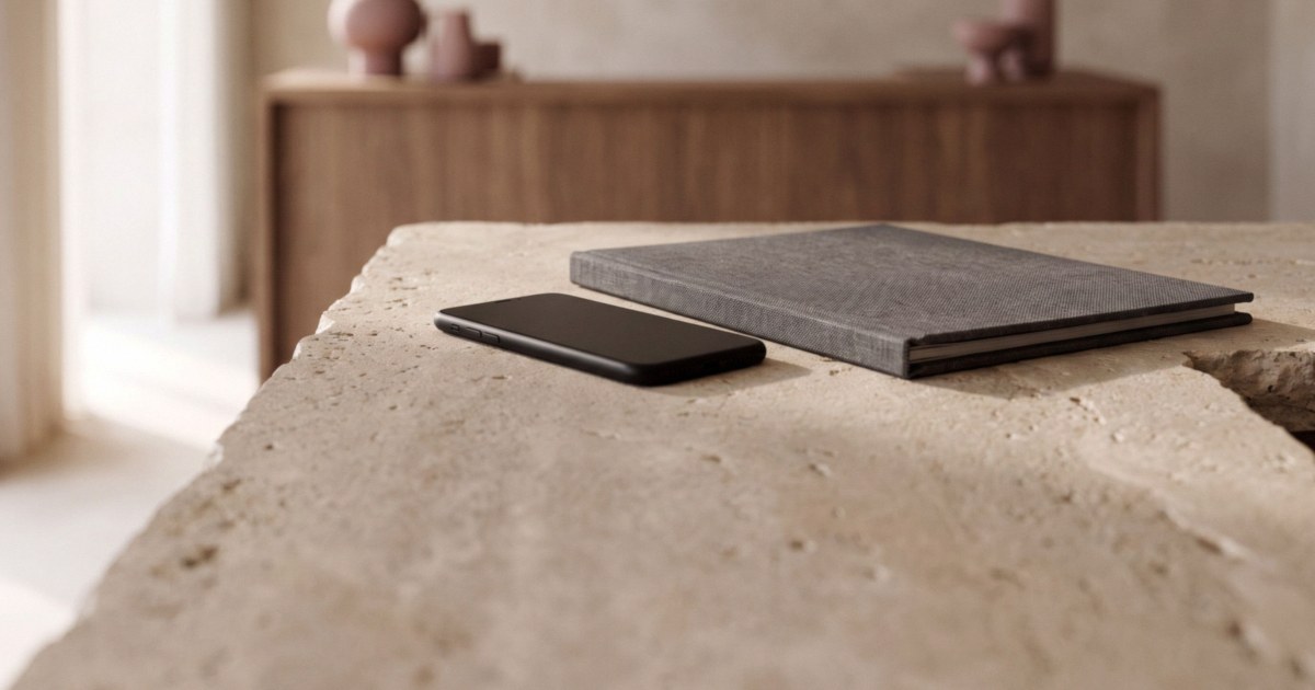 A smartphone lying face down beside a closed charcoal folder on a pale stone counter in soft daylight.